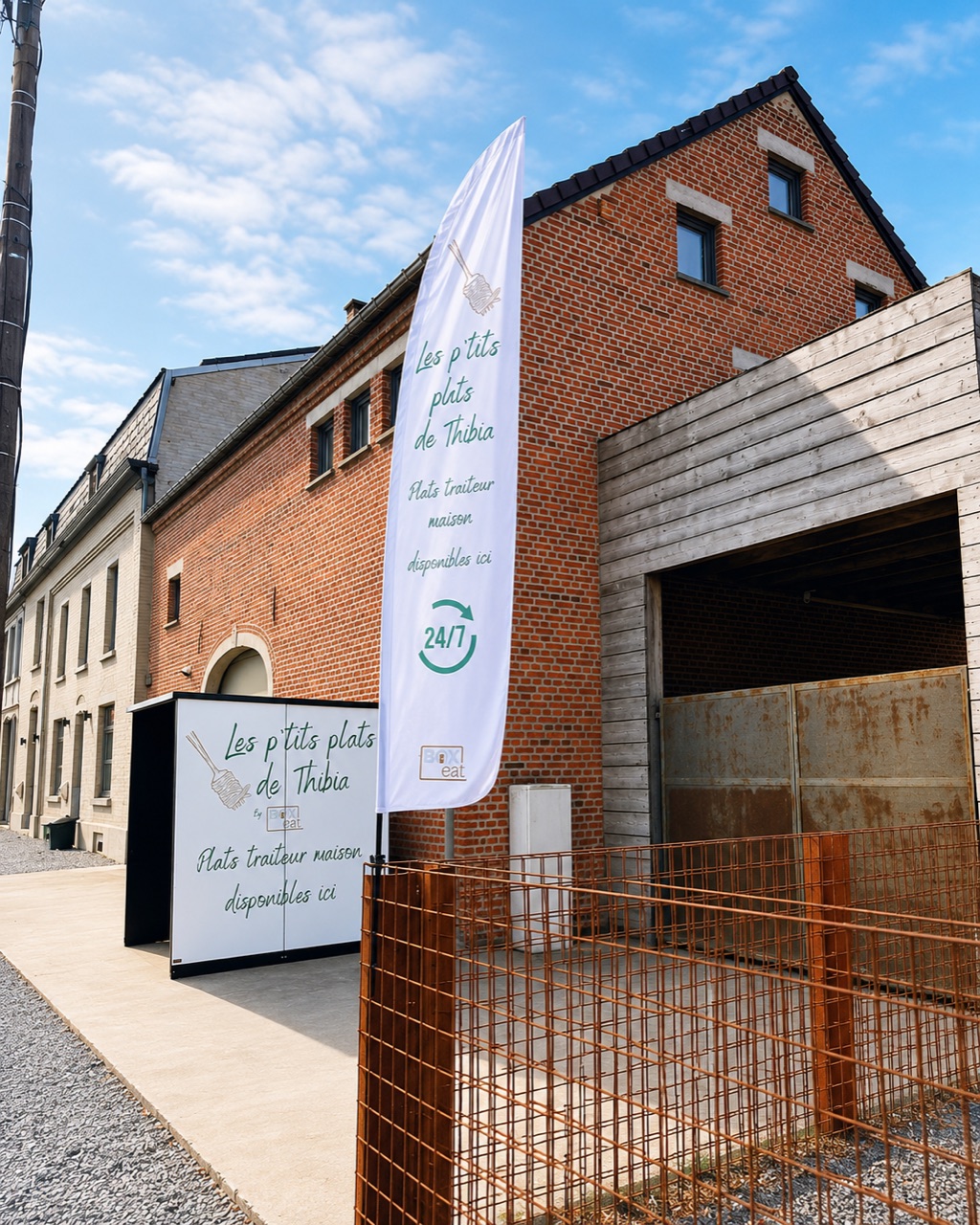 Le distributeur Les p'tits plats de Thibia de Sart-Saint-Laurent, devant le bâtiment en briques avec la bannière de la marque